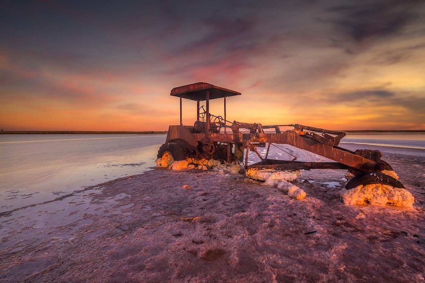 Salt scraping machinery on pink salt lake under a glowing sunset 