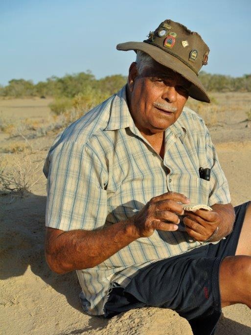 A man sits in the sand holding what looks like a piece of old bone.