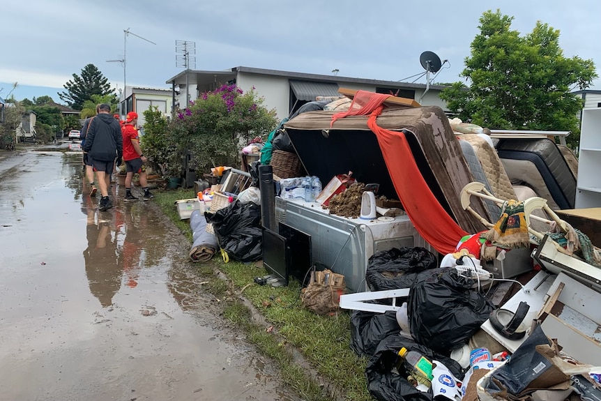 Home items like mattresses and couches piled up next to a sodden, brown street