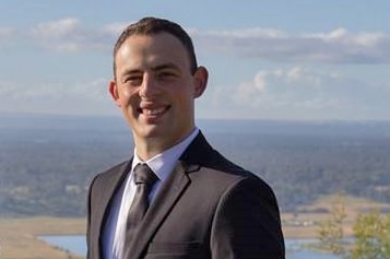 A man in a suit poses in front of a scenic view