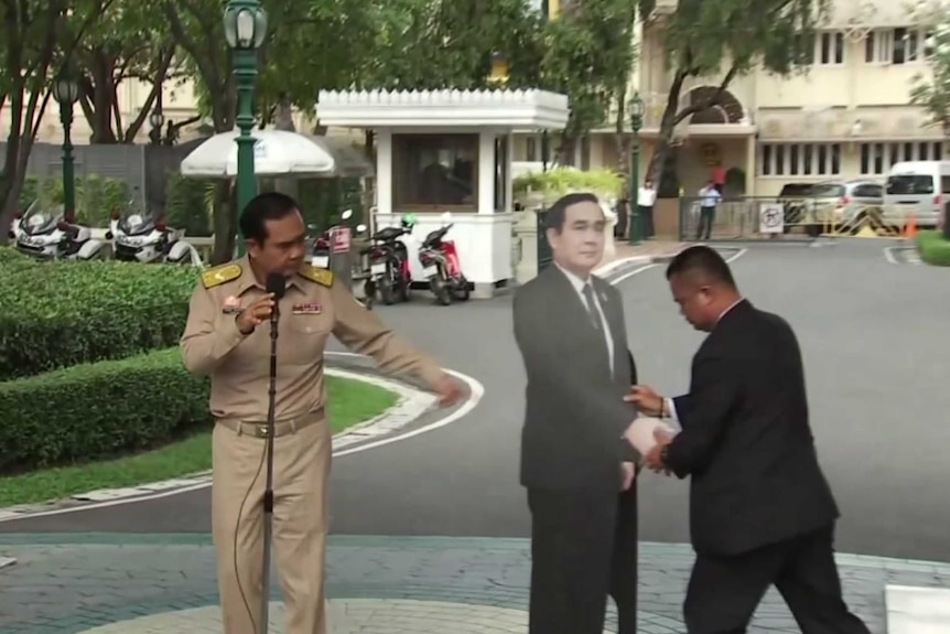 Prayuth Chan-ocha directs an assistant where to place a cardboard cut-out of himself.