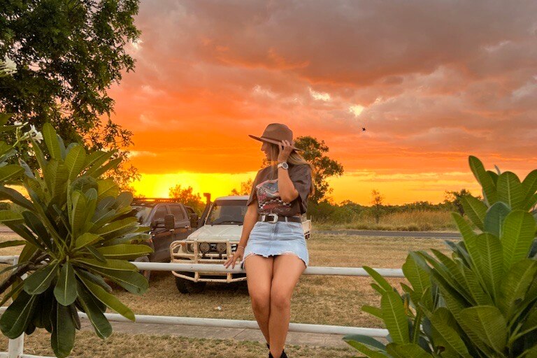 A young blonde woman watches a spectacular outback sunset.
