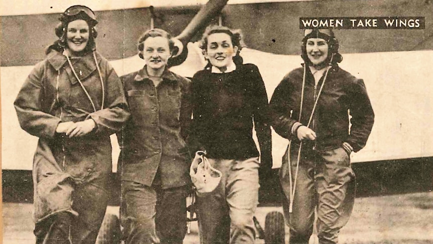 A black and white photo of four women in pilot attire linking arms, smiling