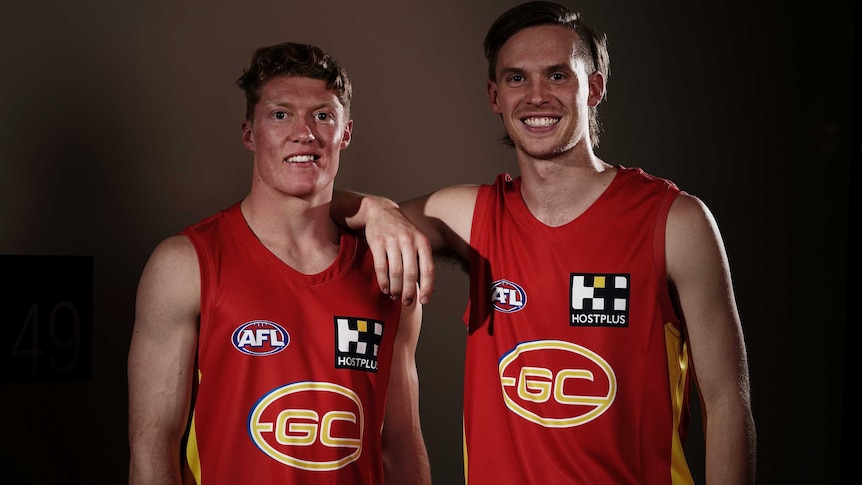 Noah Anderson rests his arm on Matt Rowell's shoulder as they smile for a shot in Gold Coast Suns jerseys.