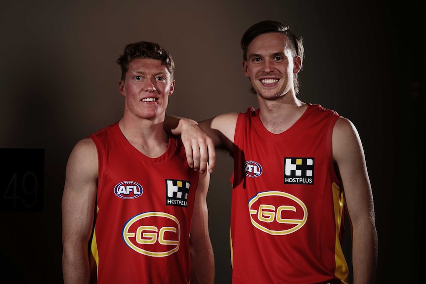 Noah Anderson rests his arm on Matt Rowell's shoulder as they smile for a shot in Gold Coast Suns jerseys.