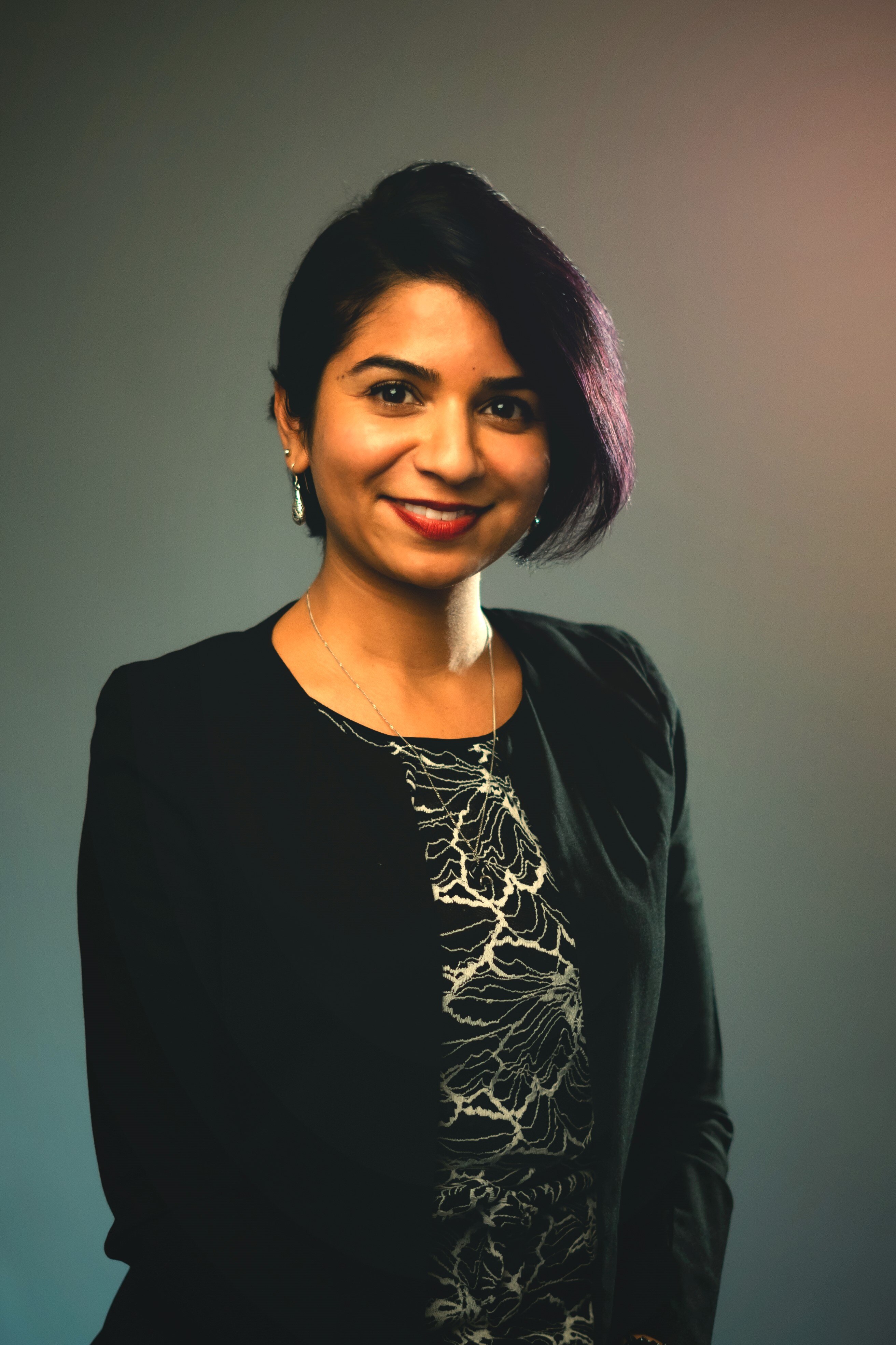 Ketvi Roopnarian stands smiling. She's wearing a patterned top and a black jacket.