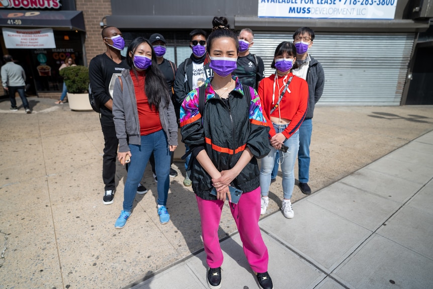 A group of eight people standing in a group on a city street wearing purple face masks.