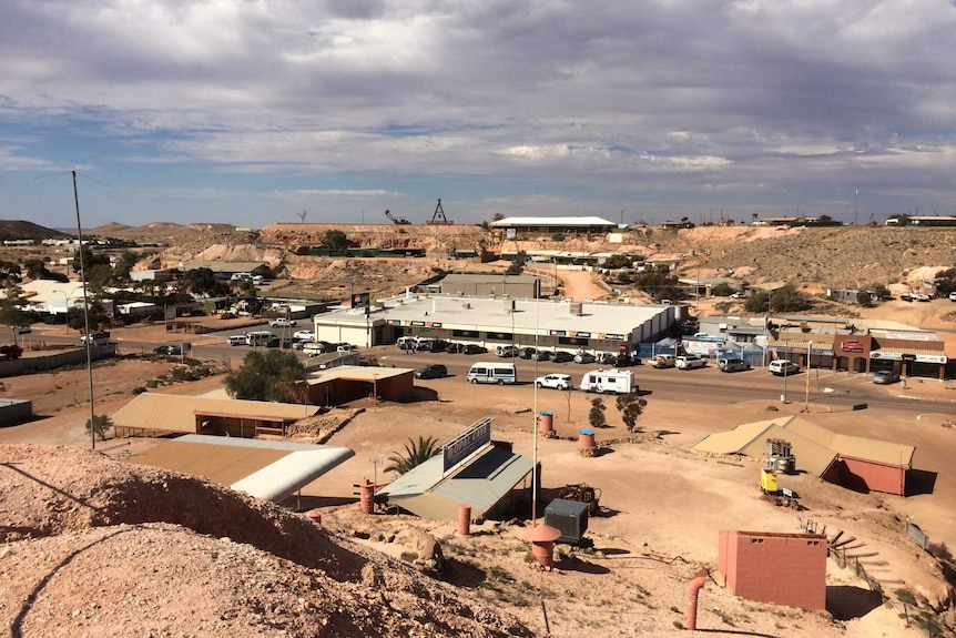 A collection of buildings built on scrubby sand hills, beneath a cloudy sky.