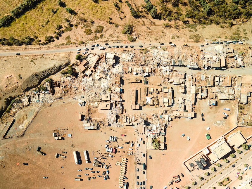 A town is seen from above, several buildings are destroyed, the landscape is covered in dust