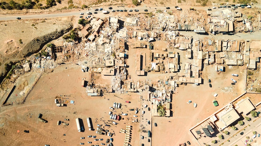 A town is seen from above, several buildings are destroyed, the landscape is covered in dust