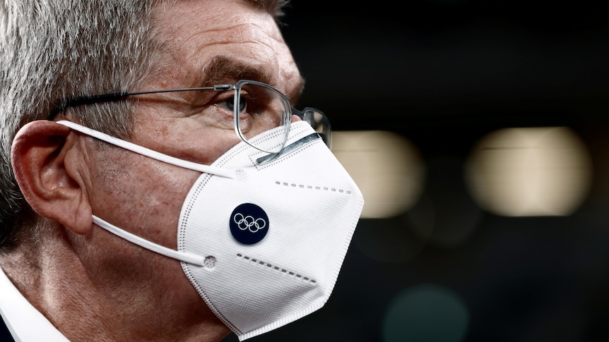 man wearing glasses and an Olympic branded face mask stares to the right.