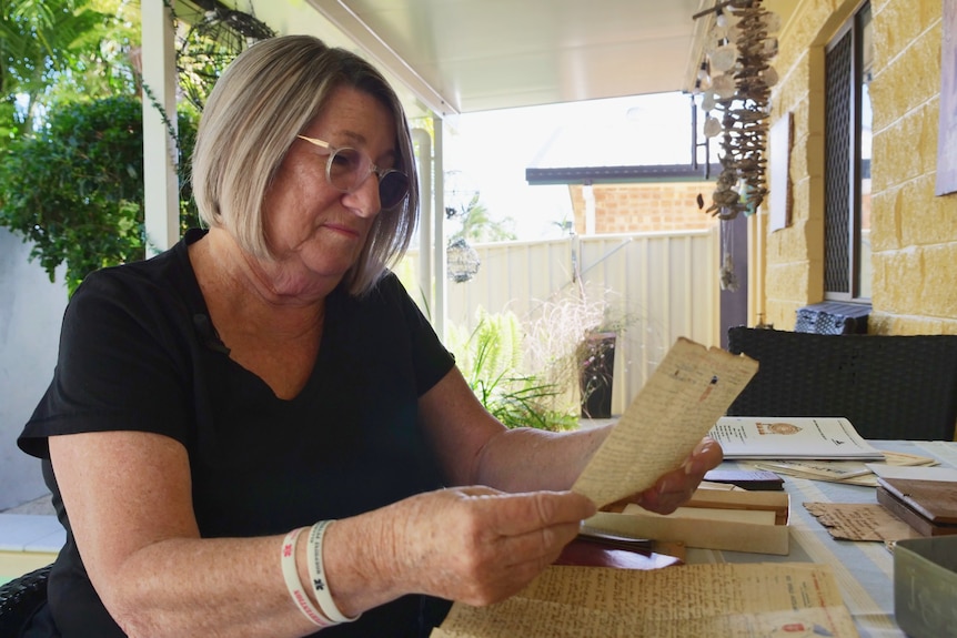 A woman sits at a table looking at an old piece of paper.