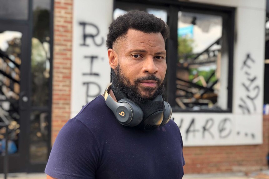 A man wearing a blue shirt and headphones around his neck stands in front of a shop in Atlanta.