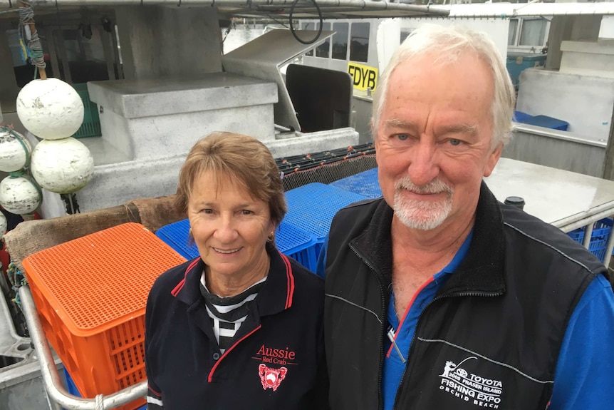 An older man and woman stand in front of stacked ice boxes, smiling.