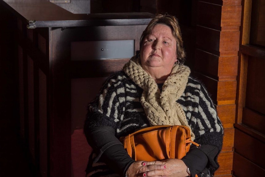 A woman sitting holding an orange handbag