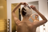 A ballerina fixes her hair while standing in front of a mirror.