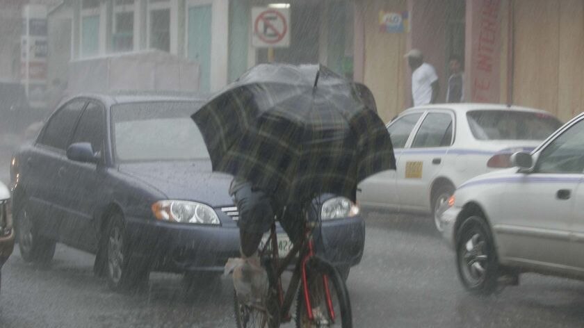 A man rides a bicycle in the rain along a street in Honduras.