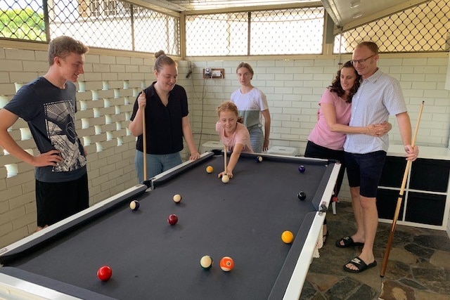 Children and two adults, who are embracing, play pool. 