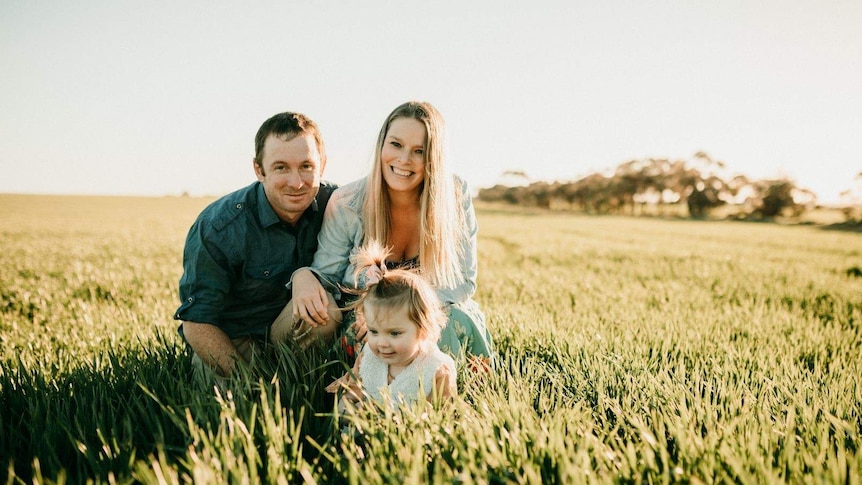 Rebecca kneeling in a field with her husband and young daughter.