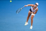 A tennis player jumps off the ground as she swings her racquet through for a serve in a match.