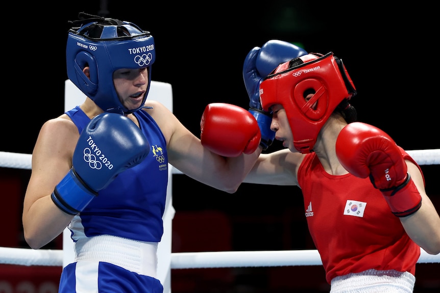 A woman wearing blue boxing gloves punching another woman wearing red boxing gloves