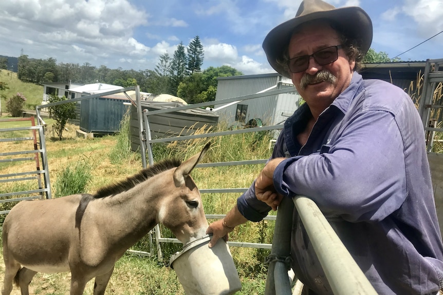 Ian smiles at the camera with a donkey eating food from his bucket.