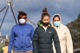 People in face masks walk over a bridge with parliament house in the background.