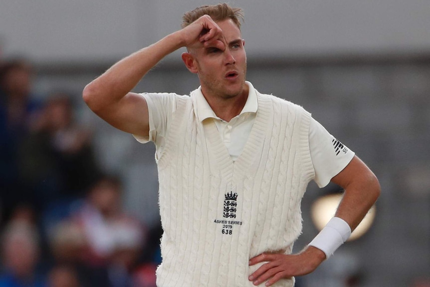 Stuart Broad stands in a sleeveless jumper with his hand on his forehead.