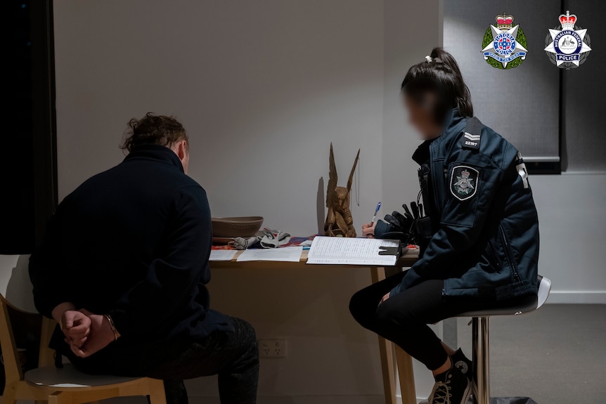 A man with his hands cuffed, next to a police officer.