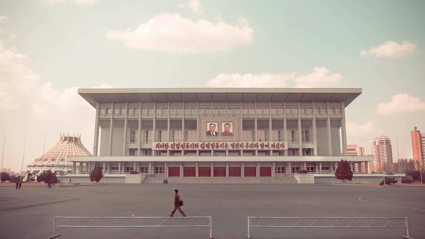 A desaturated photograph shows a stately North Korean building in the distance and a near-empty square in front of it.