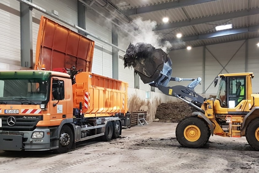 A tractor loads rich compost into a waiting truck from a pile stored in a big warehouse