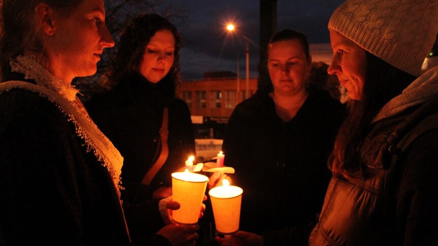 Four people hold candles at a vigil for Eurydice Dixon.