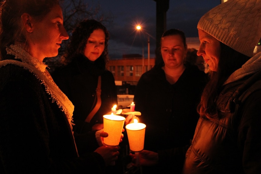 Four people hold candles at a vigil for Eurydice Dixon.