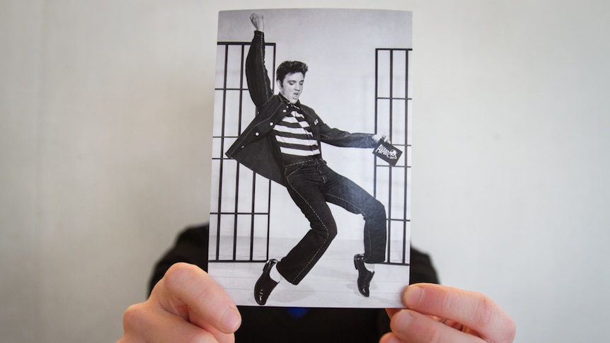 A person holds an Elvis postcard.