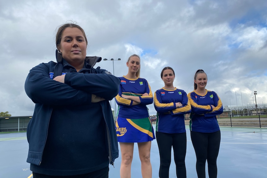 A group of netballers stand on a court with their arms crossed.