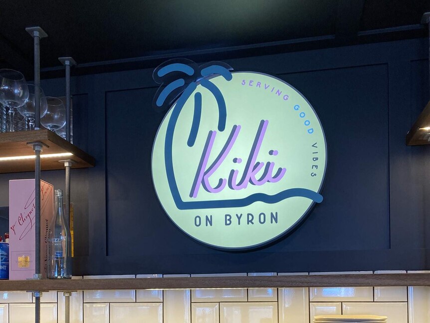 A retro-style sign featuring a palm tree says 'Kiki on Byron: serving good vibes'.