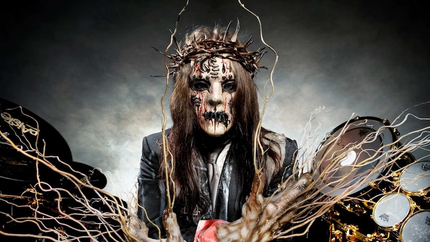 Joey Jordison wears make up and a crown of thorns as he sits as a drumkit with twiggy branches emanating from his hands