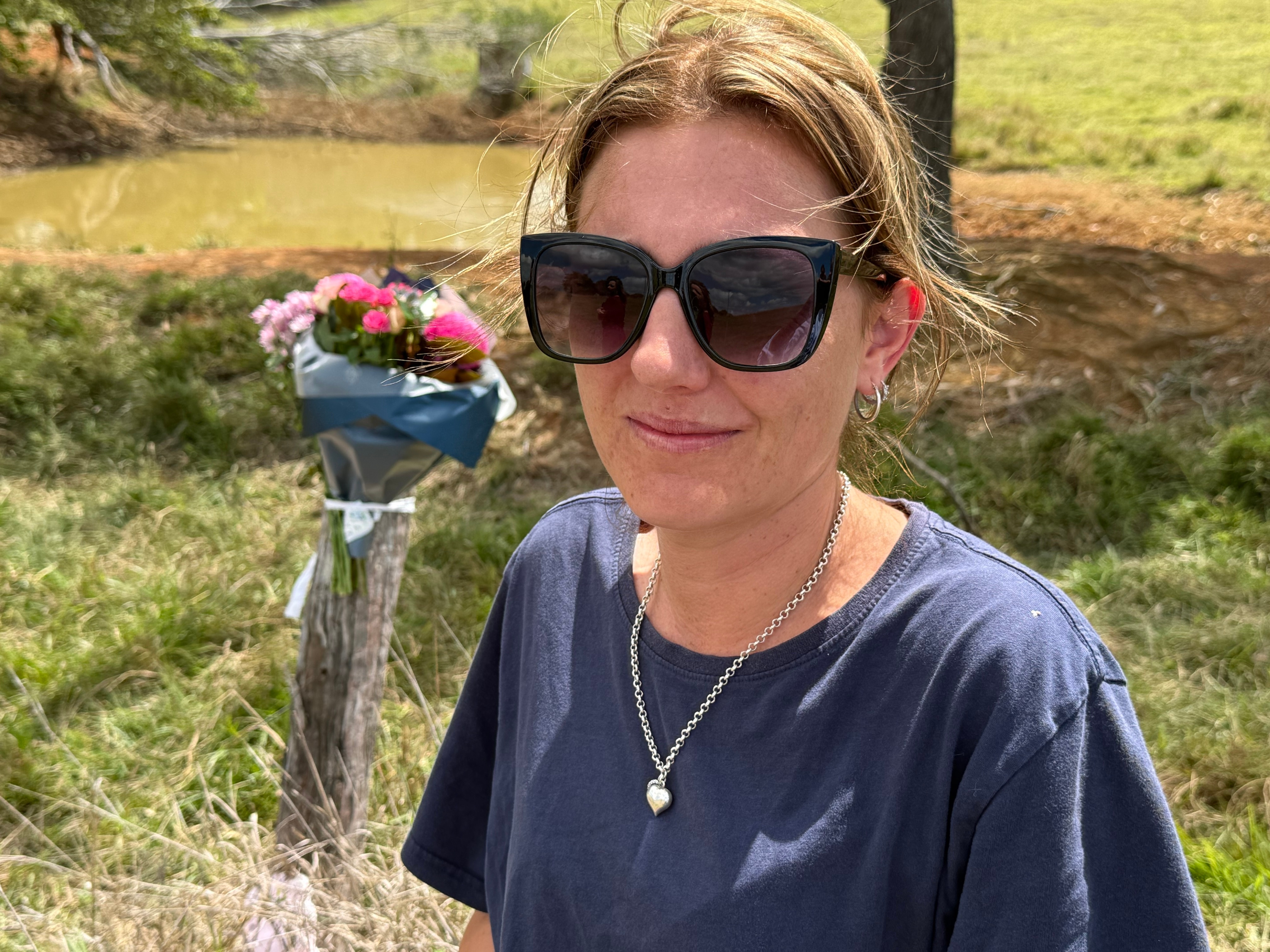 A woman with sunglasses stares solemnly in front of a bunch of flowers.