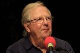 Tim Brooke-Taylor in front of a radio microphone recording an episode of I'm Sorry I Haven't a Clue.