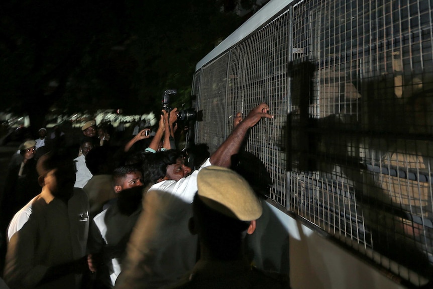 People grab at caging around a vehicle that is carrying suspects to court.