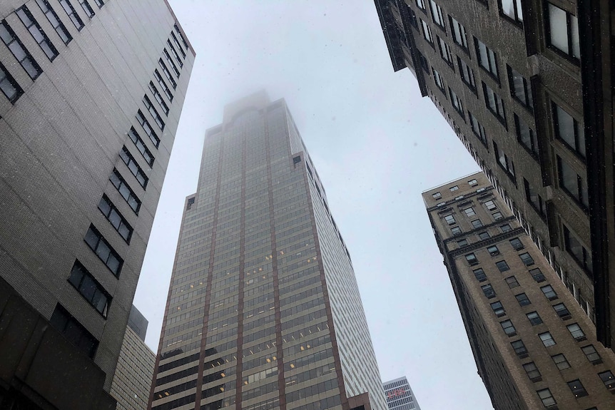 The top of a grey skyscraper covered in fog and smoke.
