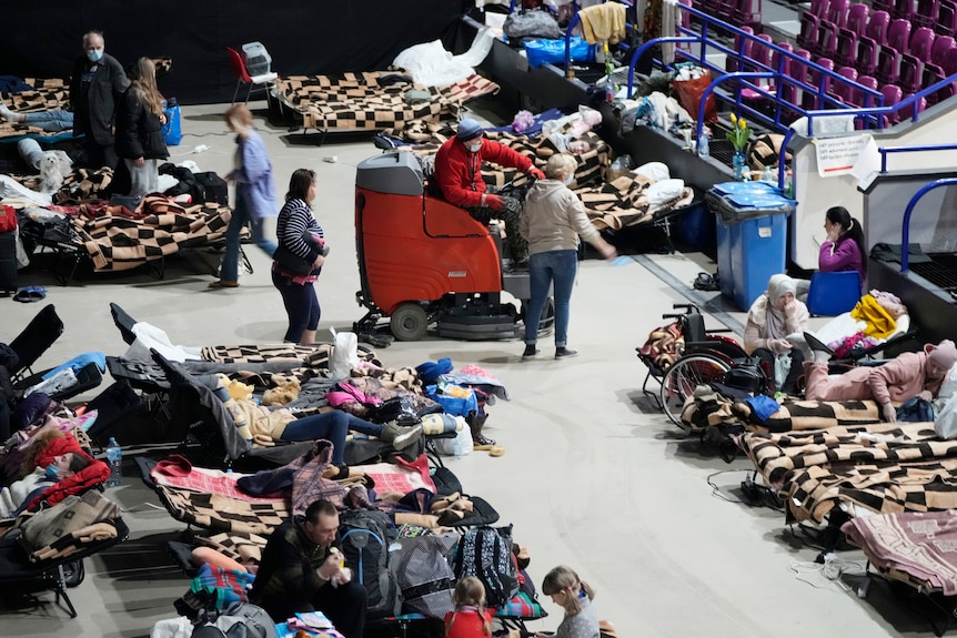 People sit and lie on portable camp beds next to a set of bleachers. 