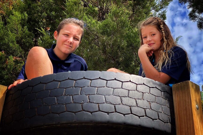 Two students sit on top of some play equipment made out of a large care tire.