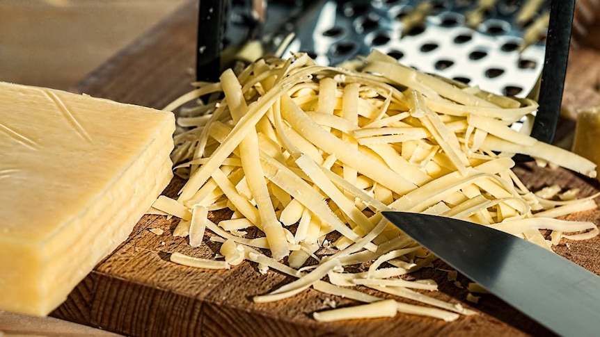 A pile of grated cheese on a chopping board with the original block of cheese next to it.