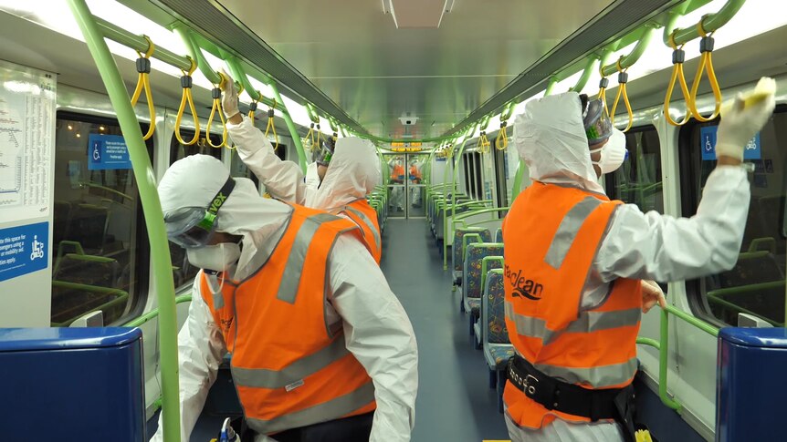 People in orange high-vis vests and PPE equipment sanitise a train carriage.