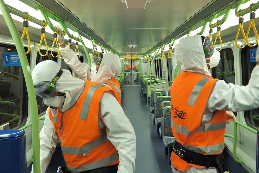 Des personnes portant des gilets haute visibilité orange et des équipements EPI désinfectent un wagon de train.