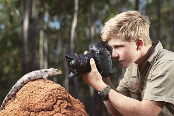 Robert Irwin holding a camera, taking a photo of a lizard