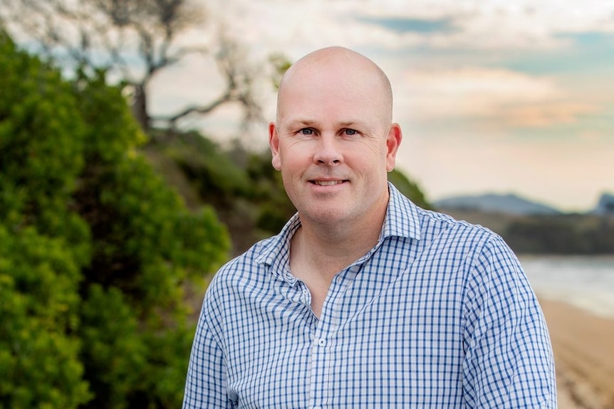 Shane Broad looks at the camera while near a beach.