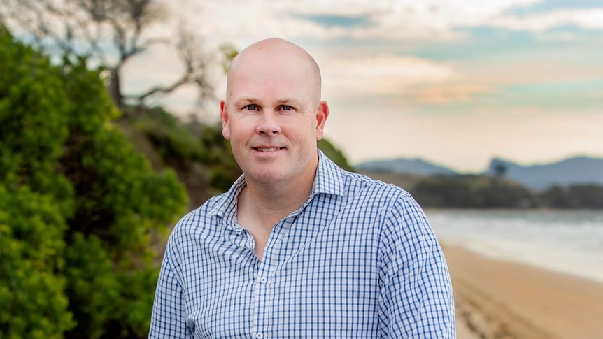 Shane Broad looks at the camera while near a beach.