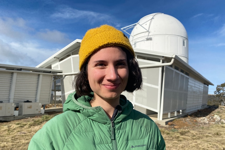 Katie Vandorou smiling, standing outside the Harlingten Telescope at Greenhill Observatory.